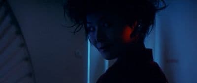 a woman standing in a dark room with a neon light on her face
