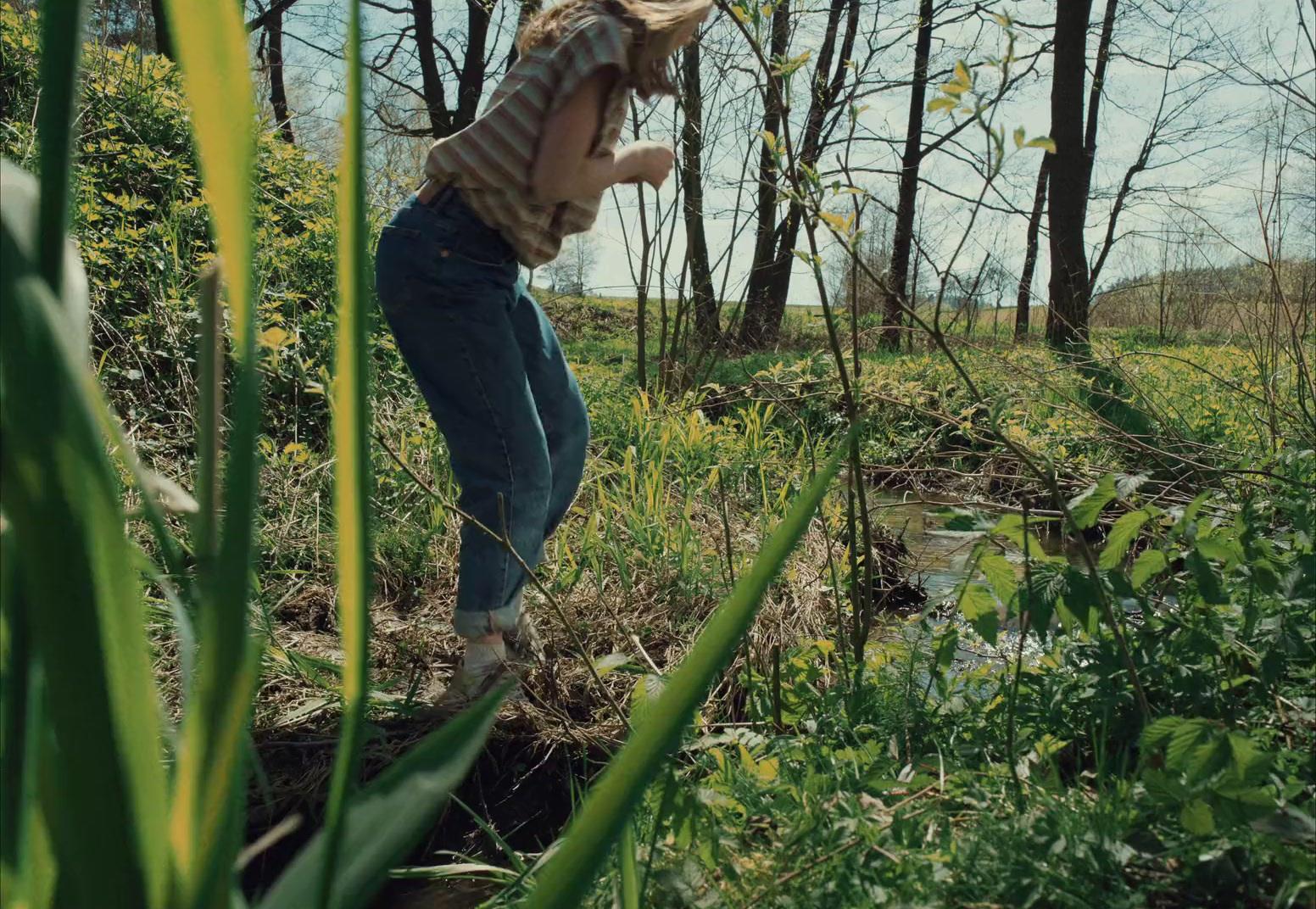a woman standing in a field next to a forest