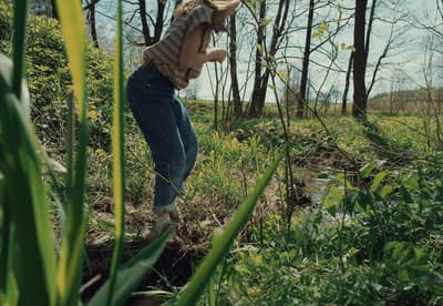 a woman standing in a field next to a forest