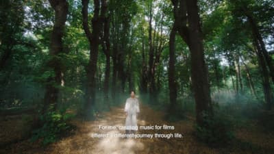 a woman in a white dress walking through a forest
