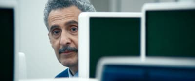 a man with a mustache looking at a computer monitor