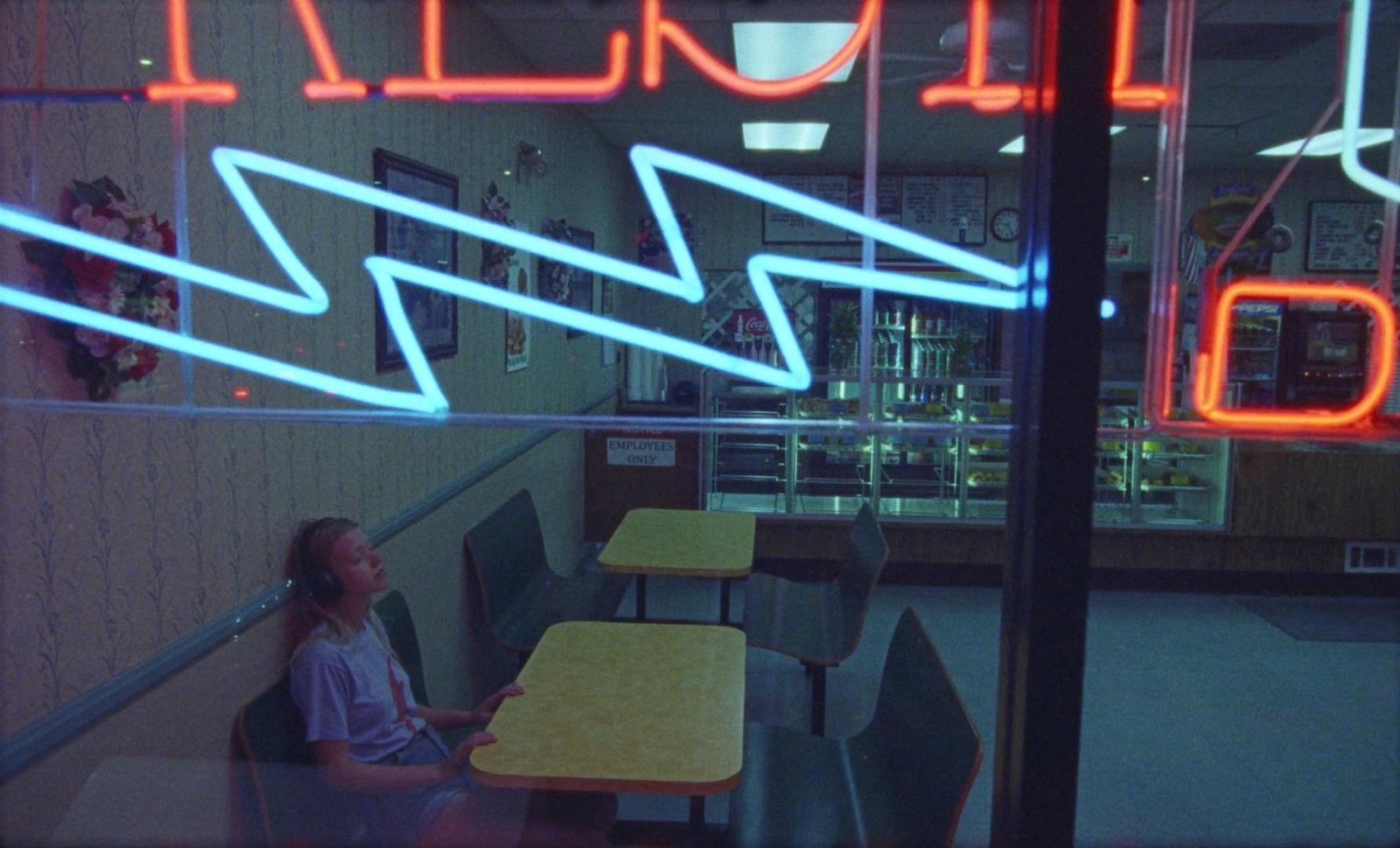 a woman sitting at a table in front of a neon sign