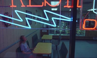 a woman sitting at a table in front of a neon sign