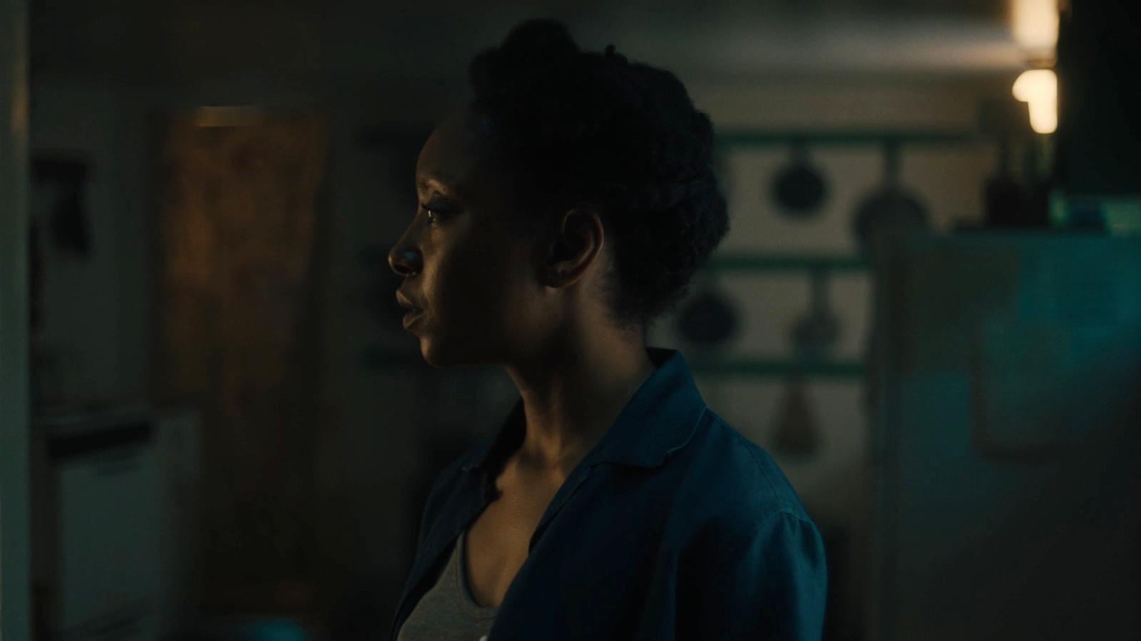 a woman standing in a dark kitchen looking off into the distance