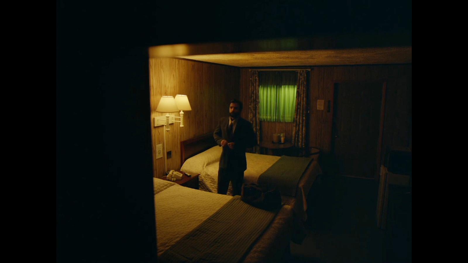 a man standing in a dark room next to two beds