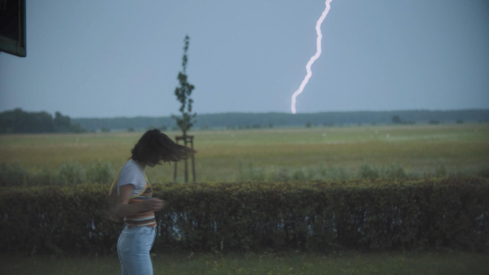 a woman standing in a field with a lightning bolt in the background