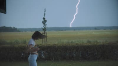 a woman standing in a field with a lightning bolt in the background