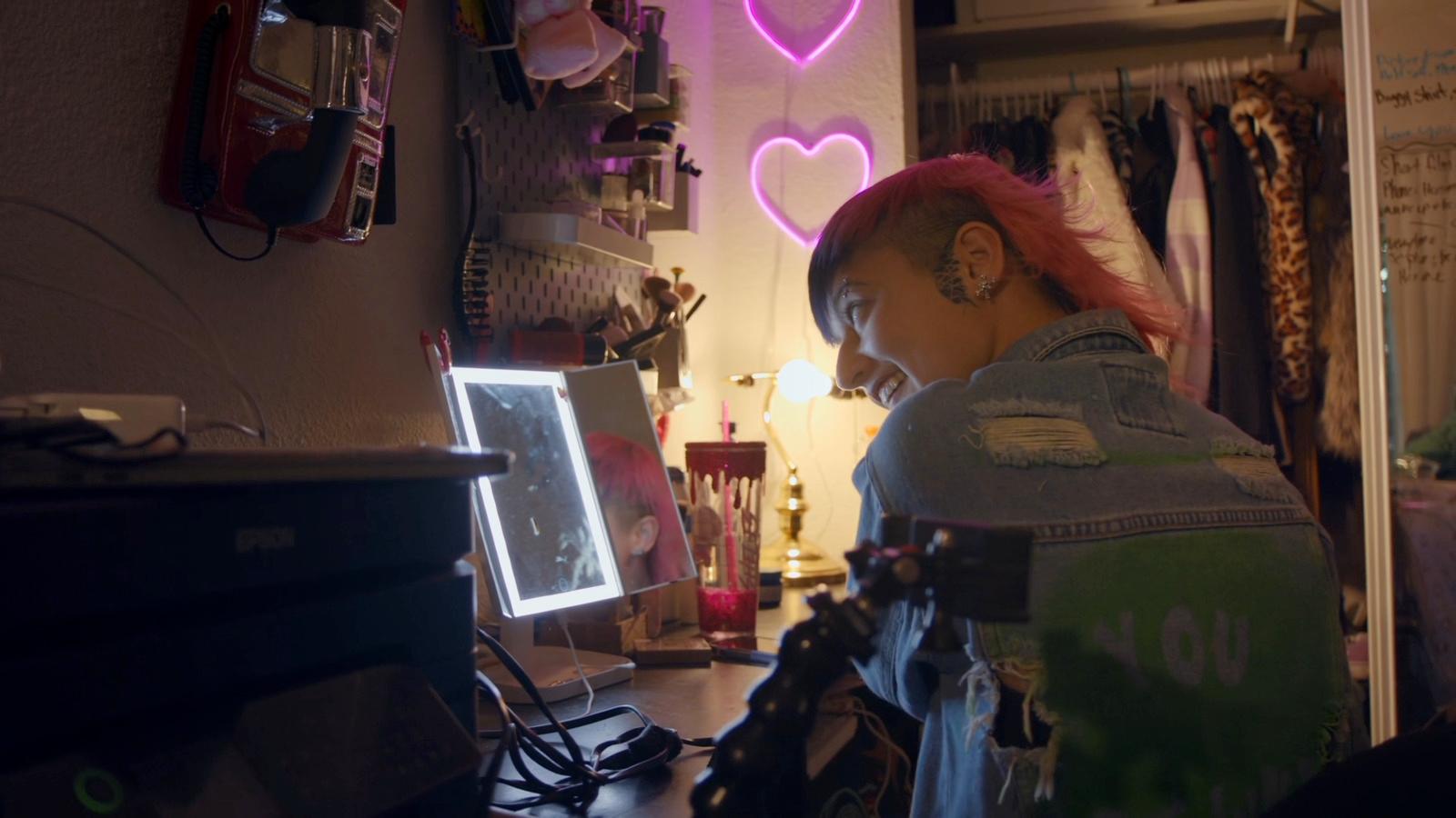 a woman with pink hair looking at a computer screen