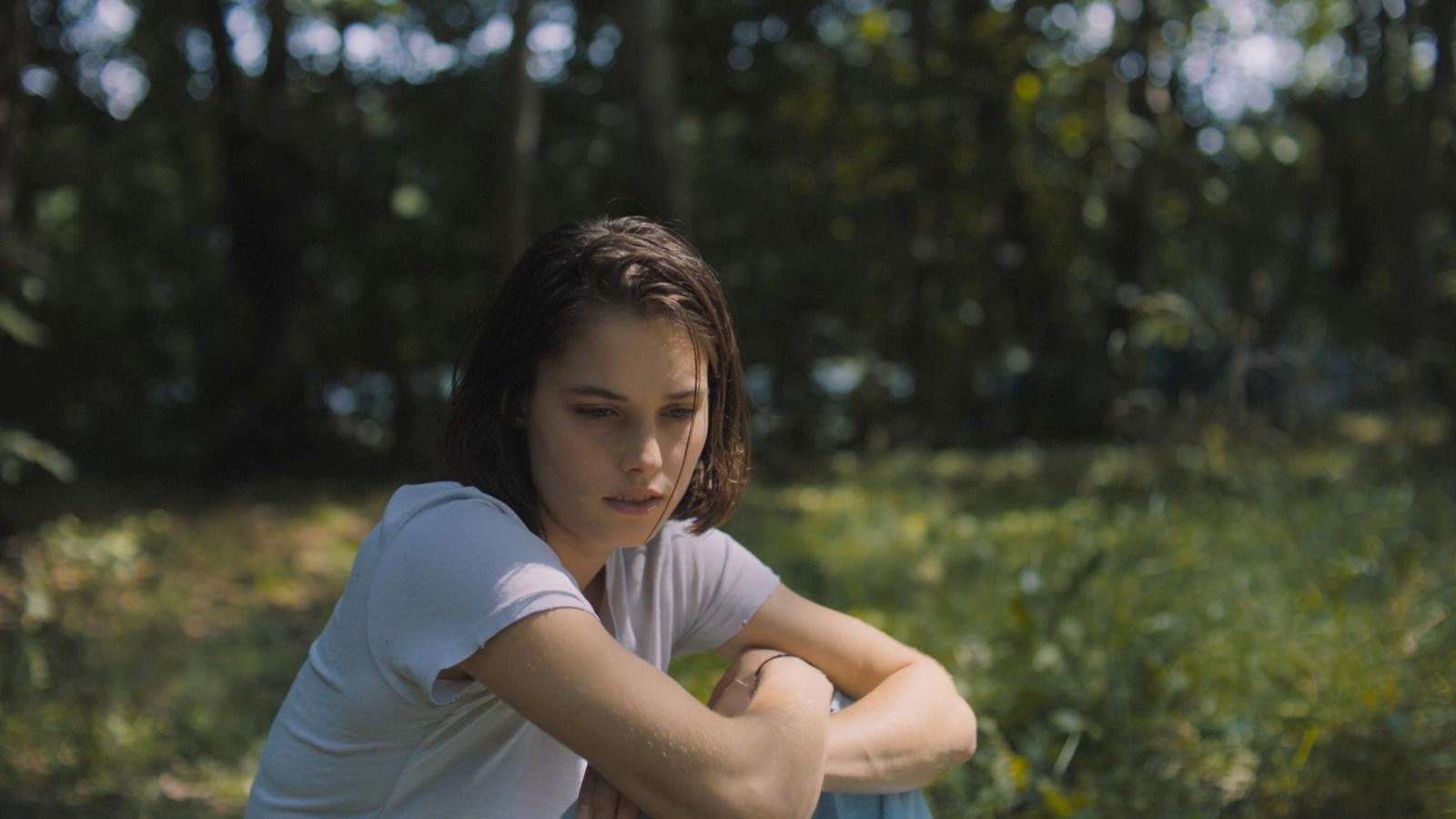 a girl sitting in the grass with her arms crossed