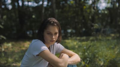 a girl sitting in the grass with her arms crossed