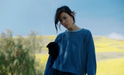 a woman standing in a field with a tree in the background