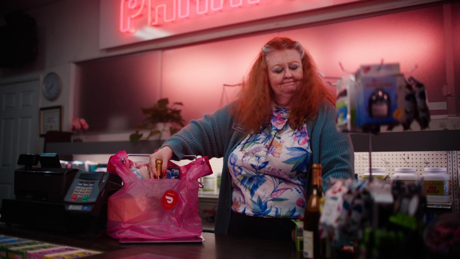 a woman standing at a counter with a pink bag