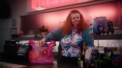 a woman standing at a counter with a pink bag