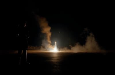 a person standing in the dark with a rocket in the background