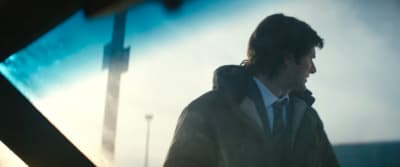 a man in a jacket and tie walking down a street