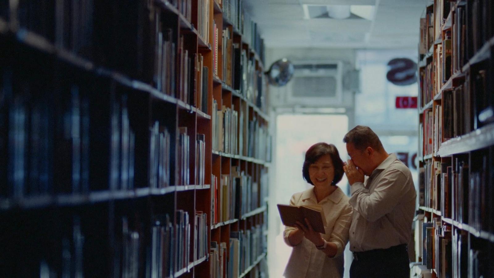 a man and woman standing in a library looking at a book