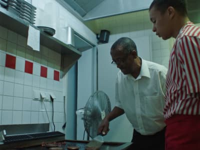 two men in a kitchen preparing food on a grill