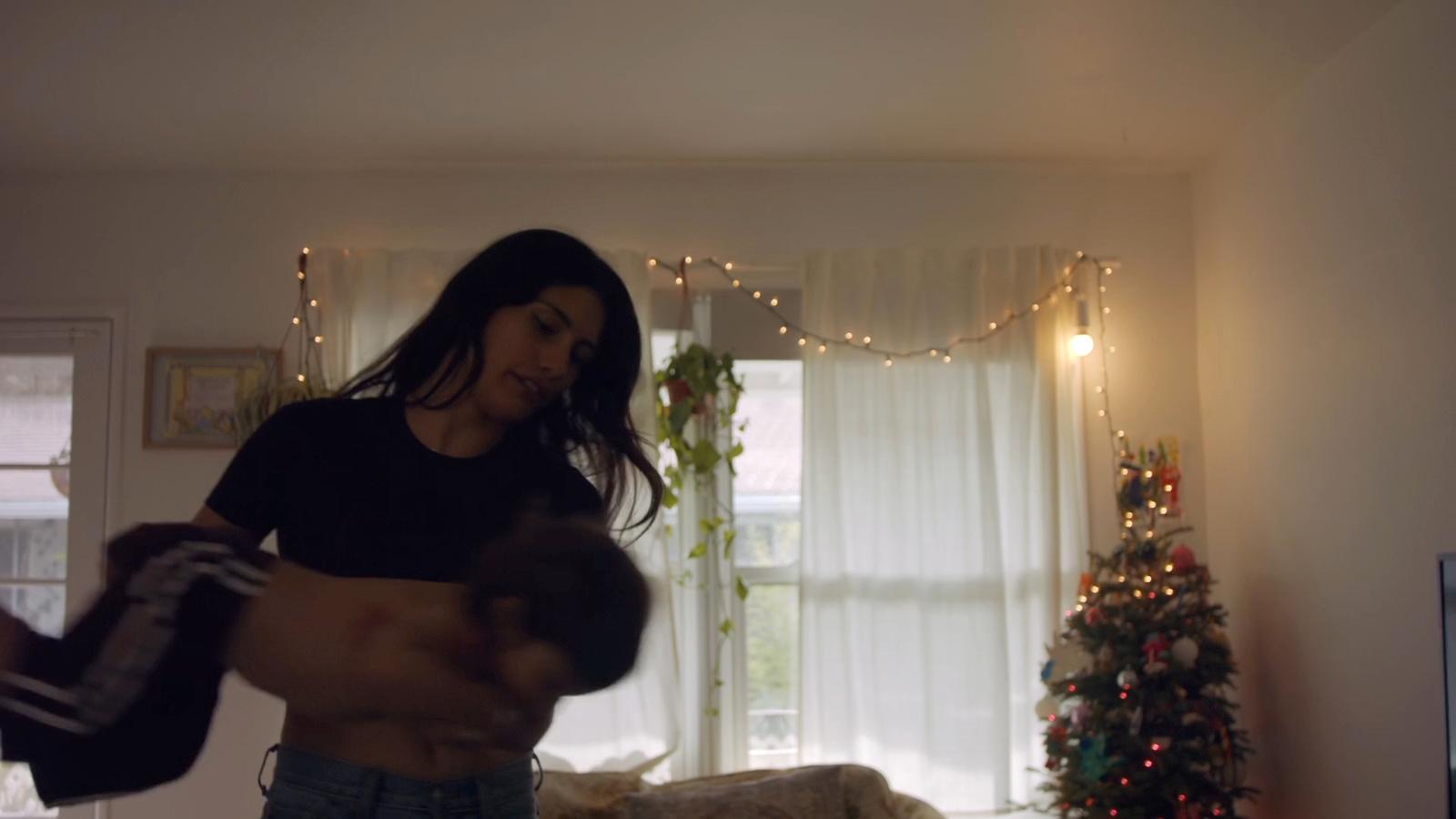 a woman standing in a living room next to a christmas tree