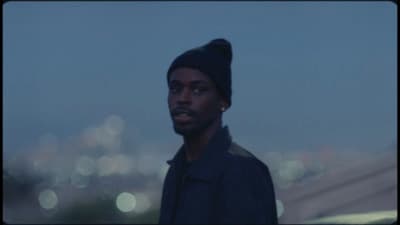 a man with a beanie standing in front of a cityscape