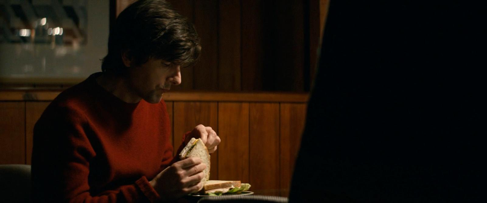 a woman sitting at a table eating a sandwich