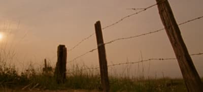 a fence with barbed wire and the sun in the background