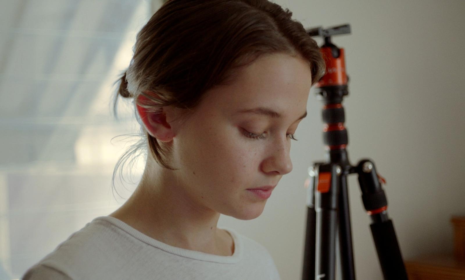 a woman looking down at a camera next to a tripod