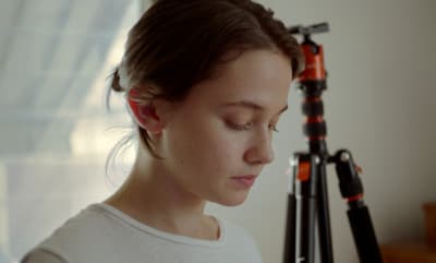 a woman looking down at a camera next to a tripod