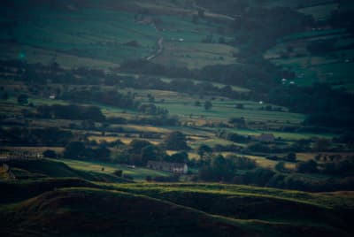 a view of a lush green hillside with a house in the distance