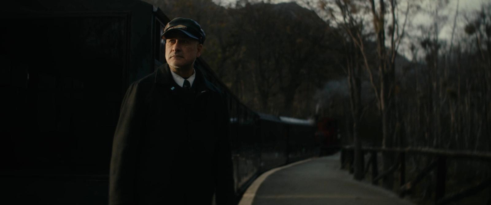 a man in a coat and hat standing next to a train