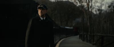 a man in a coat and hat standing next to a train