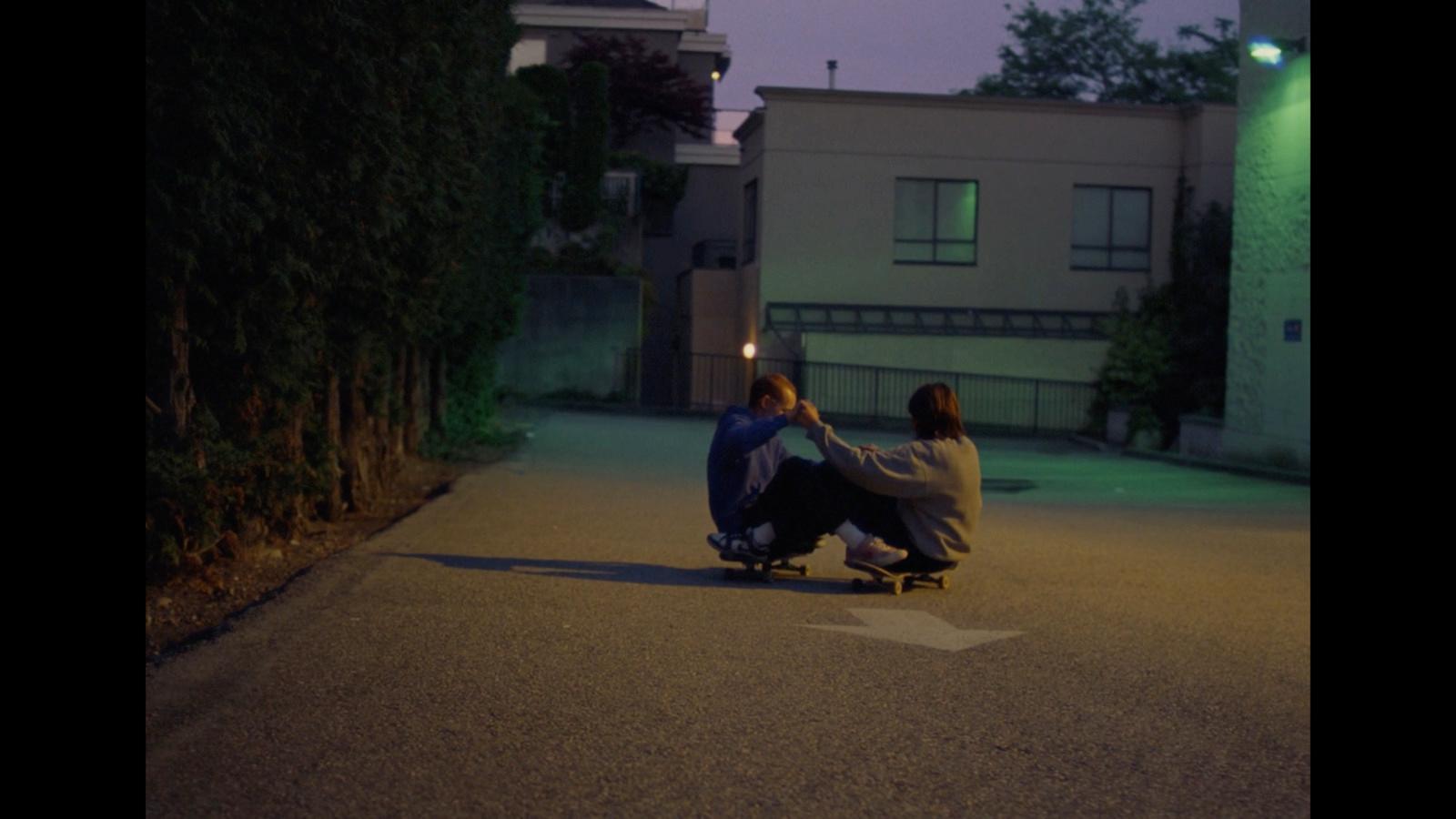 two people sitting on a skateboard in the street