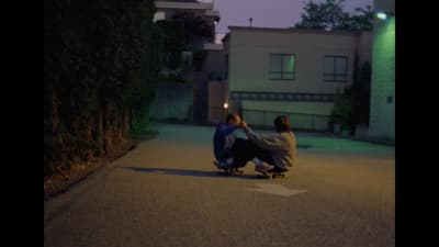 two people sitting on a skateboard in the street