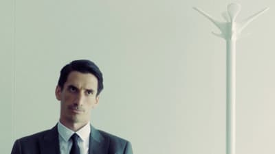 a man in a suit and tie standing in front of a lamp