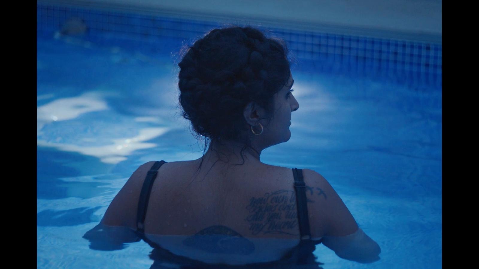 a woman sitting in a pool with a tattoo on her back