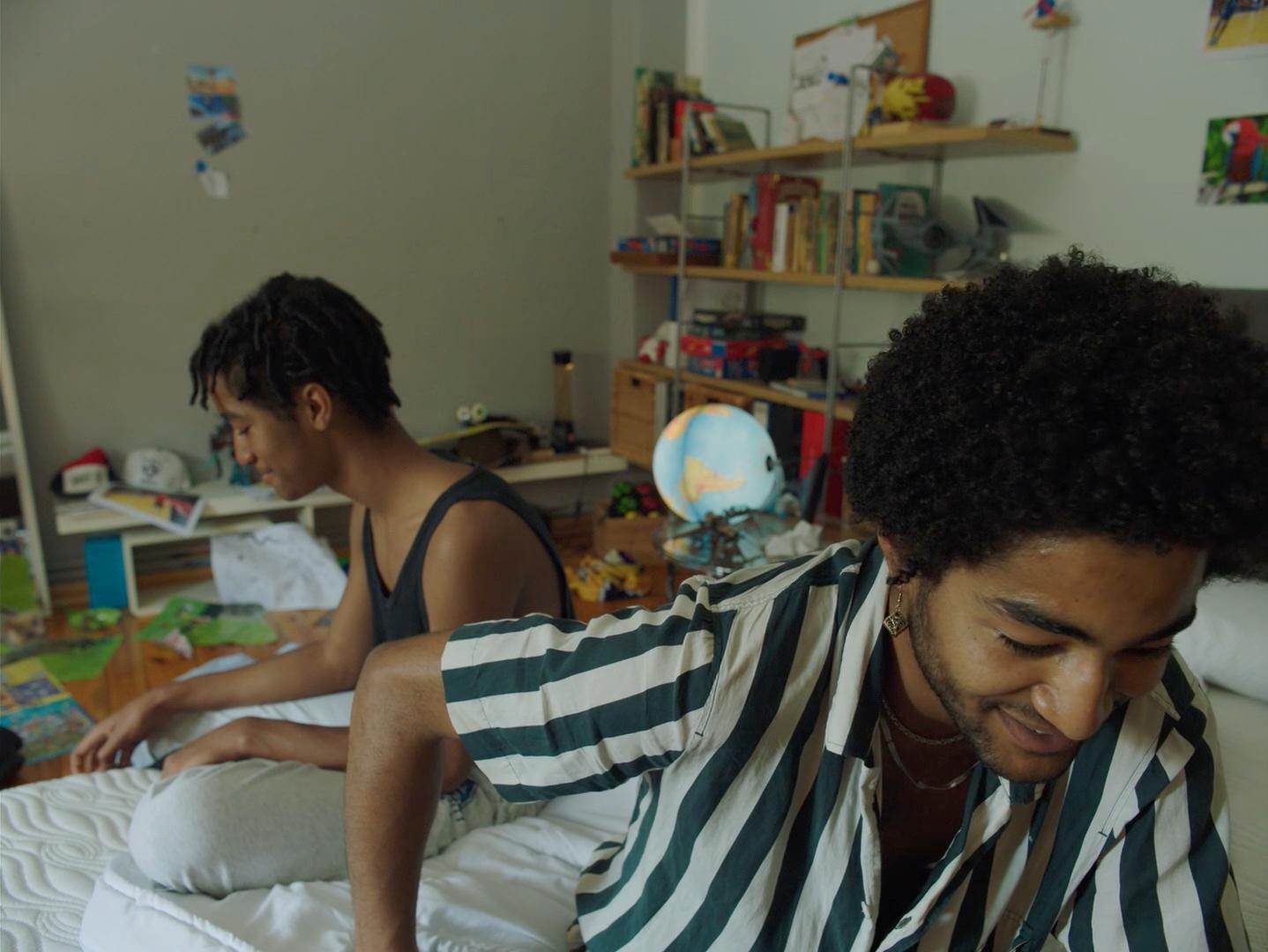 a man sitting on top of a bed next to another man