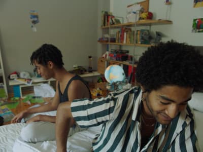 a man sitting on top of a bed next to another man