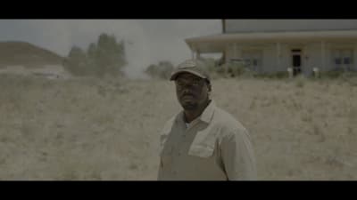 a man standing in a field with a house in the background