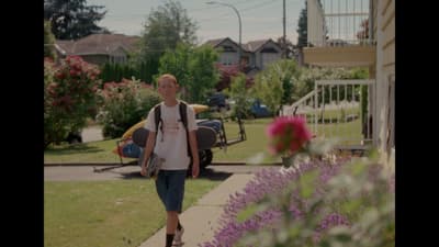 a man walking down a sidewalk next to a flower garden