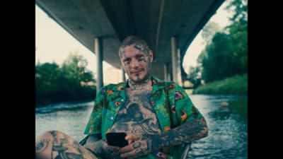 a man with tattoos sitting under a bridge