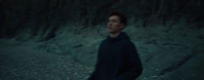 a man in a black hoodie standing in front of a mountain