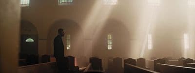 a man standing in a church with sunlight streaming through the windows