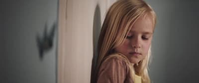 a young blonde girl leaning against a wall