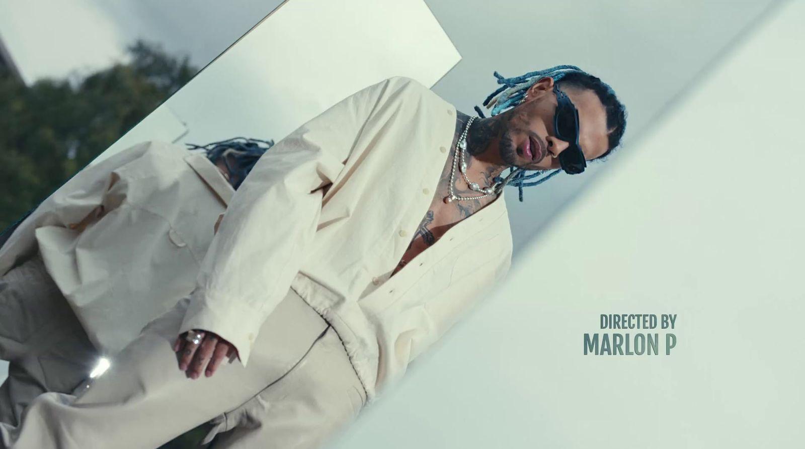 a man in a white suit and sunglasses leaning against a wall