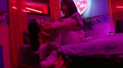 a woman sitting on a bed in a room with neon lights