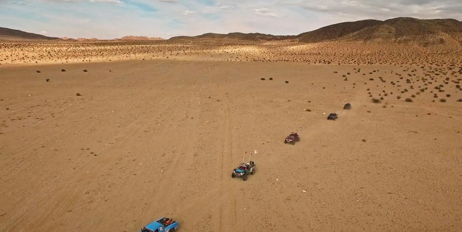 a group of four vehicles driving across a desert