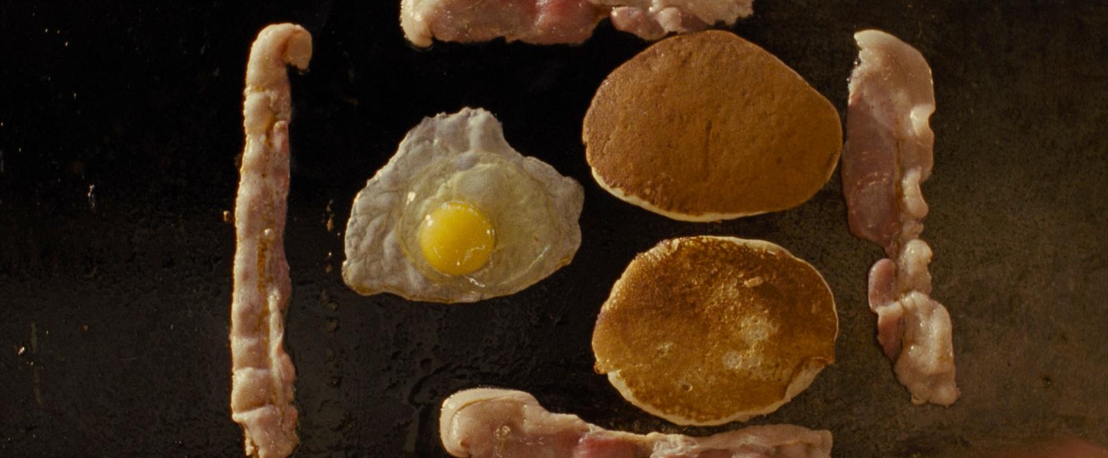 bacon, eggs, and sausages are being cooked on a grill