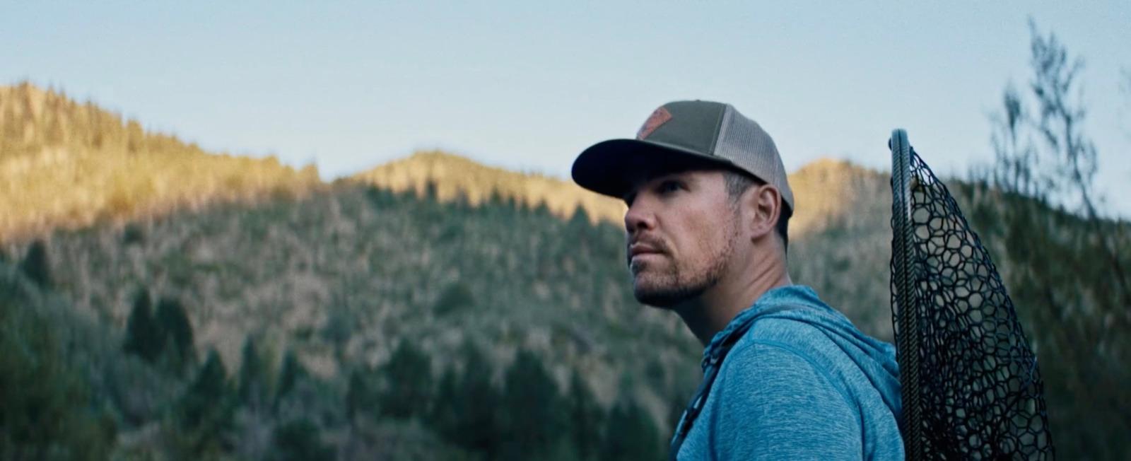 a man with a hat and a backpack in front of a mountain