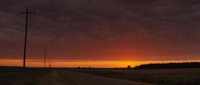 the sun is setting over a rural road