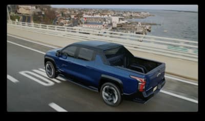 a blue truck driving down a road next to a body of water