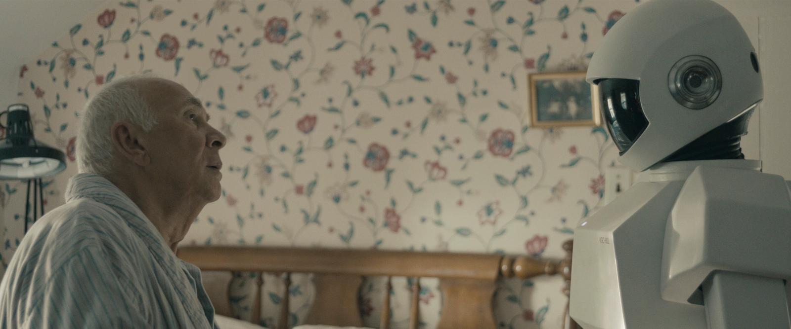 an old man sitting in a bed next to a robot